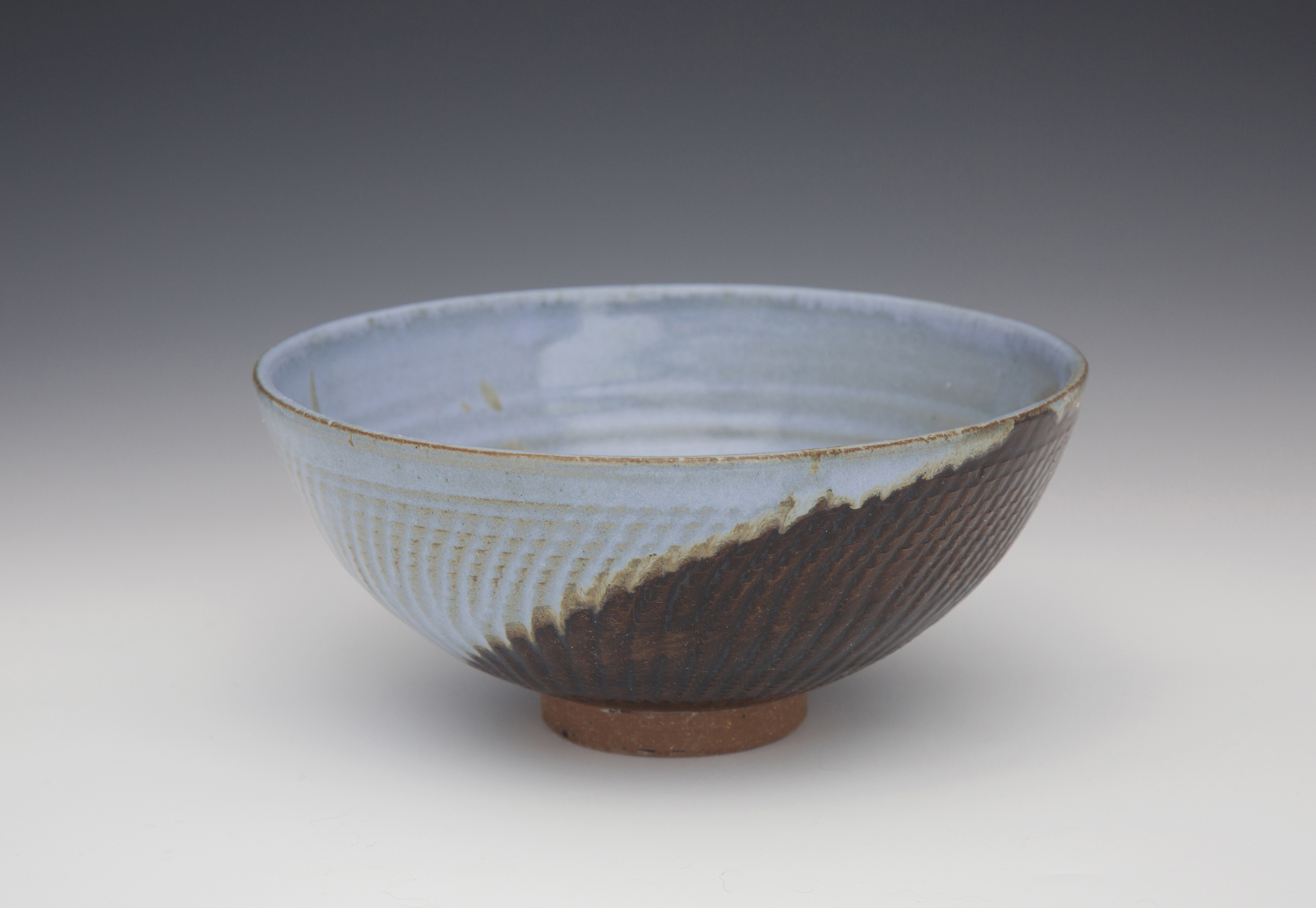 A bowl made from clay that is half light blue and half brown. It has a wooden circle as the bottom